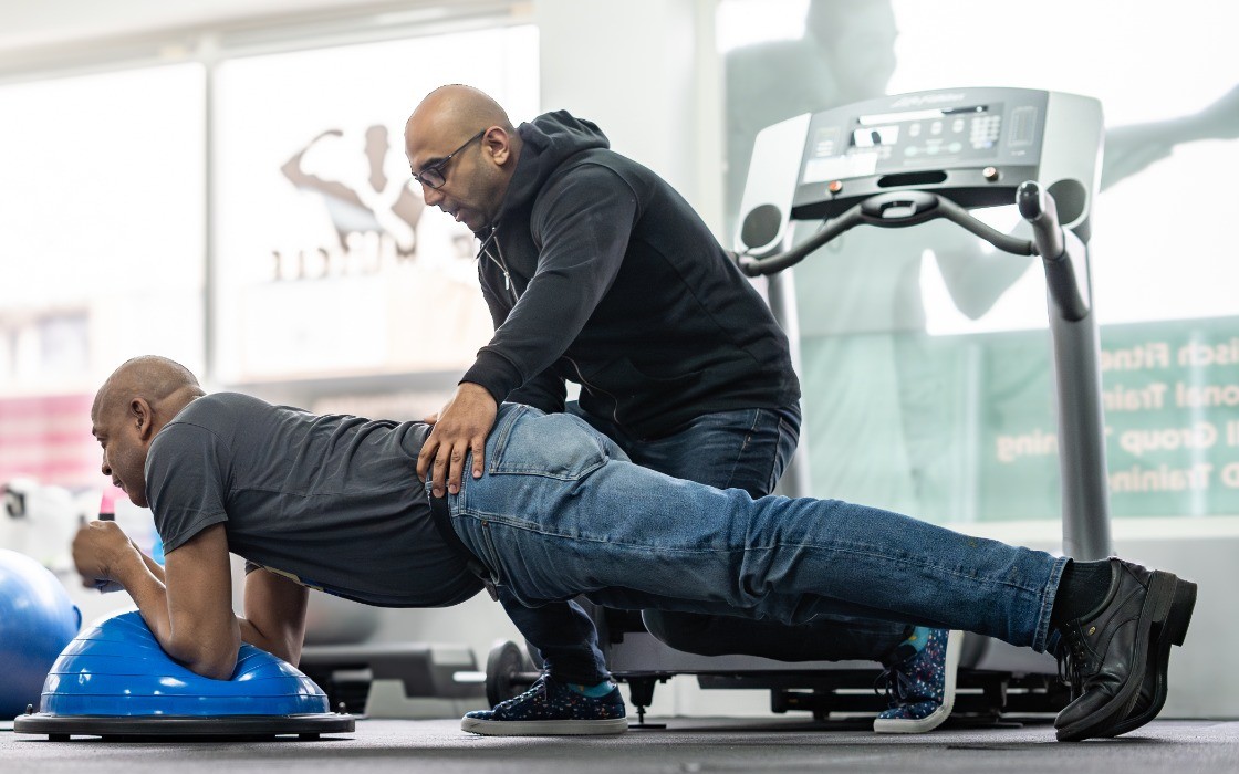 Fysiotherapeut begeleidt een patiënt bij een oefening op een balanceerpad in de sportschool van Fysiotherapie Suri in Den Helder